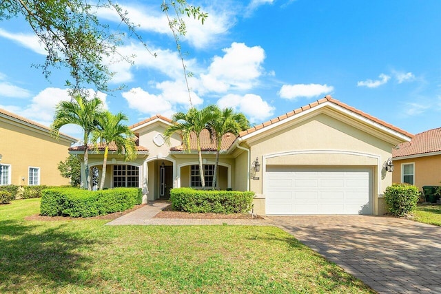 mediterranean / spanish house with decorative driveway, stucco siding, a front yard, a garage, and a tiled roof