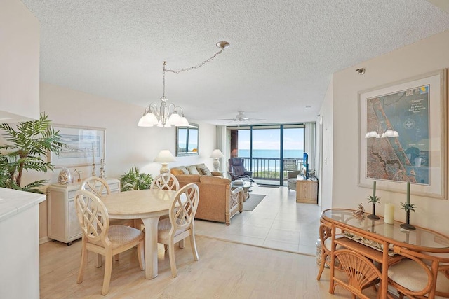 dining area featuring expansive windows, a textured ceiling, a water view, ceiling fan with notable chandelier, and light wood-type flooring