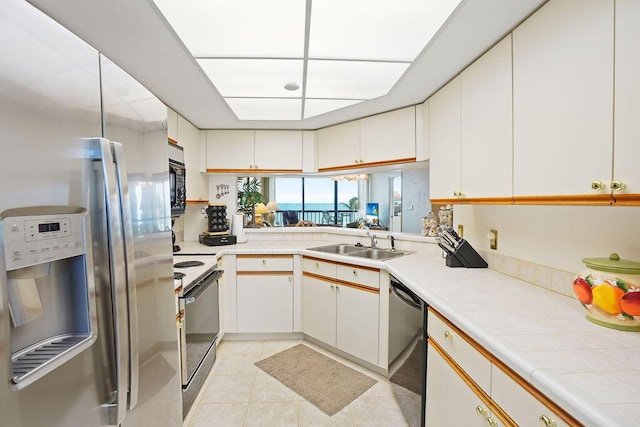 kitchen featuring sink, light tile patterned floors, kitchen peninsula, white cabinets, and black appliances