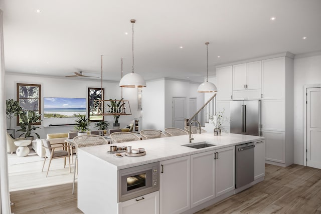 kitchen with decorative light fixtures, a center island with sink, sink, built in appliances, and white cabinetry