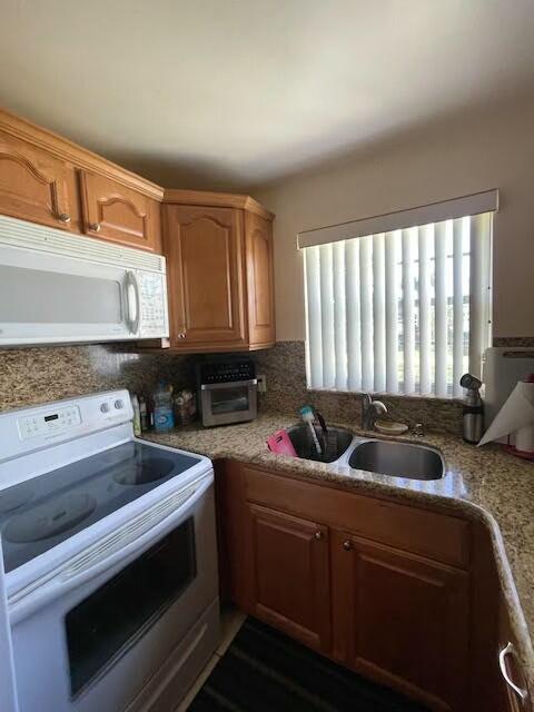 kitchen with decorative backsplash, white appliances, light stone counters, and sink