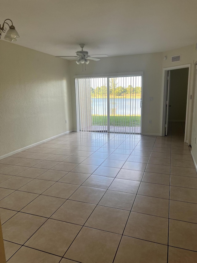 empty room featuring a water view, ceiling fan, and light tile patterned flooring