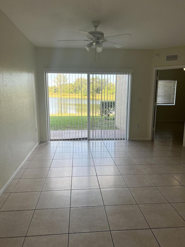 empty room featuring ceiling fan, light tile patterned flooring, and a water view