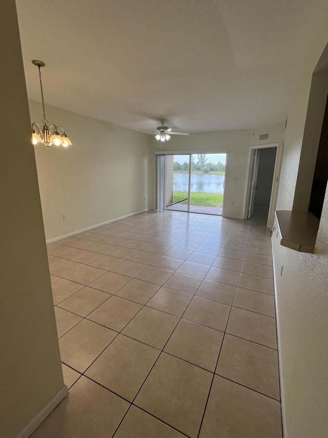 spare room featuring light tile patterned floors, ceiling fan with notable chandelier, and a water view