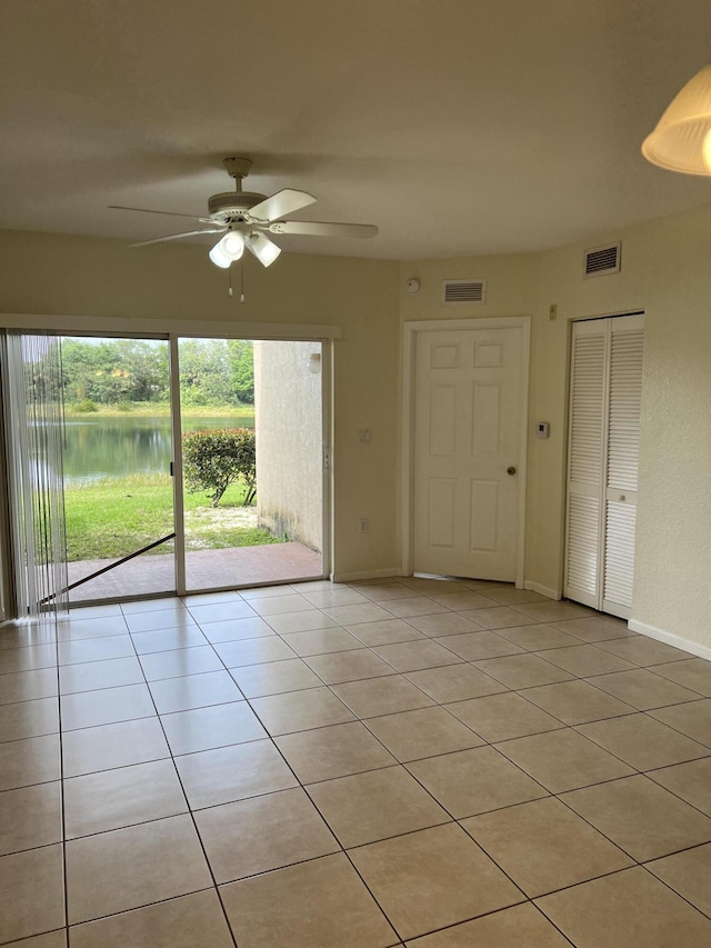 tiled empty room with ceiling fan and a water view