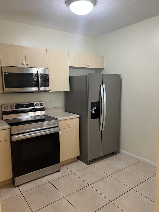 kitchen featuring light tile patterned floors, a textured ceiling, stainless steel appliances, and light brown cabinetry