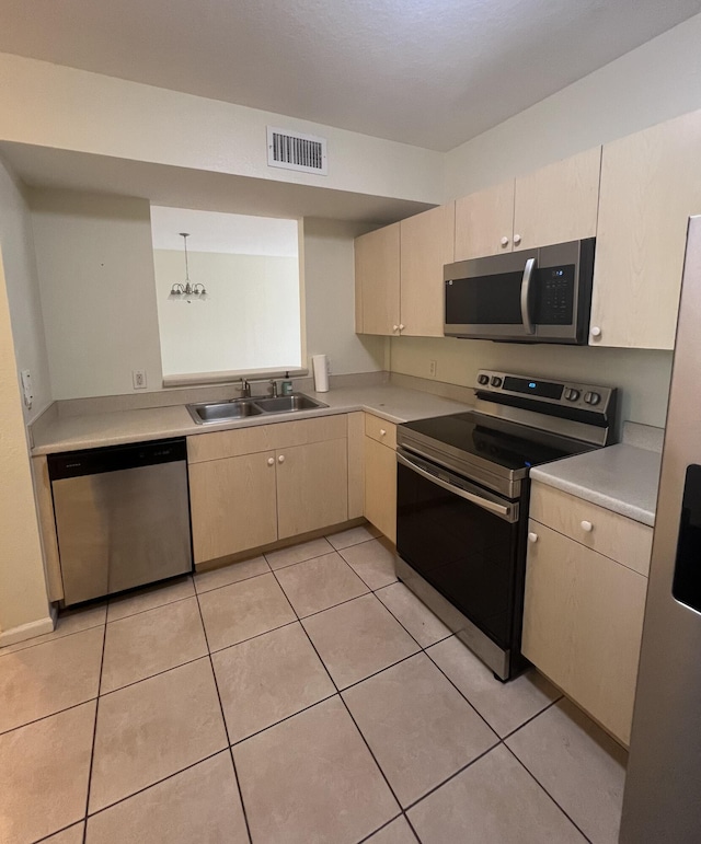 kitchen with appliances with stainless steel finishes, light tile patterned floors, hanging light fixtures, and sink