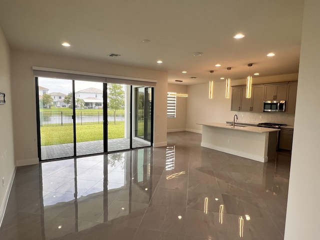 kitchen featuring a kitchen island with sink, a water view, sink, hanging light fixtures, and decorative backsplash