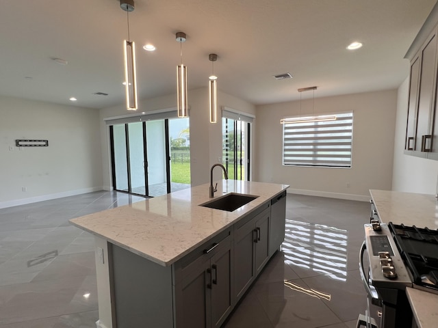 kitchen with light stone countertops, gray cabinetry, a kitchen island with sink, sink, and pendant lighting