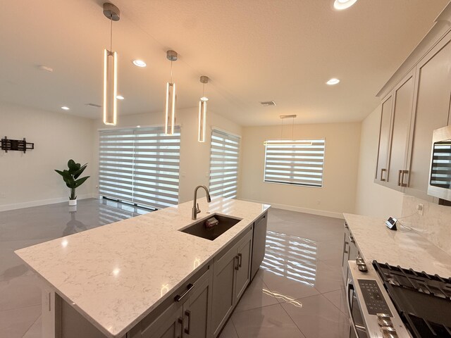 kitchen featuring pendant lighting, stainless steel gas range oven, sink, gray cabinets, and light stone counters