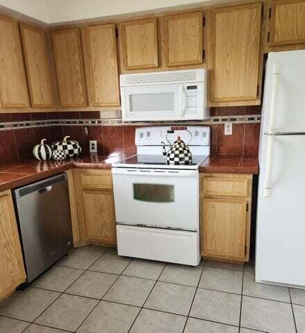 kitchen with decorative backsplash, light tile patterned flooring, and white appliances