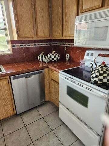 kitchen with tile counters, decorative backsplash, white appliances, and light tile patterned floors