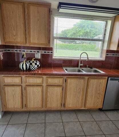 kitchen with decorative backsplash, sink, light tile patterned floors, and stainless steel dishwasher