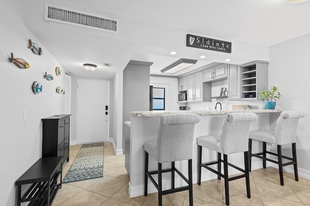 kitchen with kitchen peninsula, gray cabinets, a kitchen bar, and light tile patterned floors