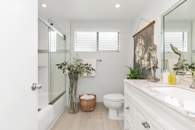 full bathroom with a wealth of natural light, shower / bath combination with glass door, vanity, and toilet