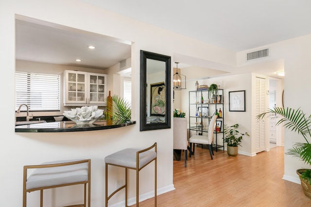 kitchen with white cabinets, decorative light fixtures, sink, kitchen peninsula, and light hardwood / wood-style flooring