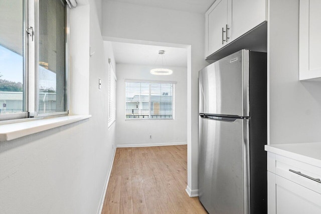 kitchen with decorative light fixtures, light wood-type flooring, white cabinetry, and stainless steel refrigerator