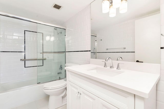 full bathroom with vanity, shower / bath combination with glass door, tile patterned floors, toilet, and tile walls