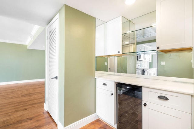 bar featuring light hardwood / wood-style flooring, white cabinetry, beverage cooler, and crown molding