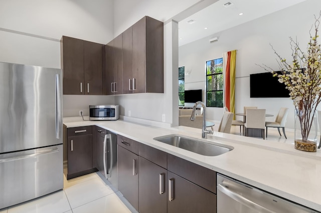 kitchen with light tile patterned flooring, appliances with stainless steel finishes, dark brown cabinetry, and sink