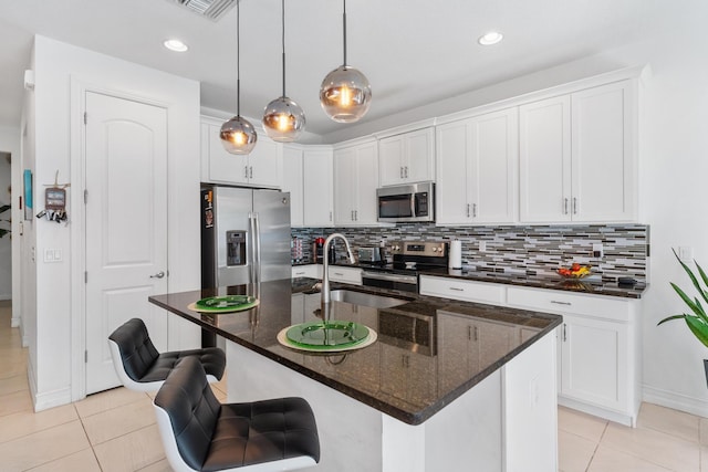 kitchen featuring light tile patterned flooring, pendant lighting, an island with sink, white cabinets, and stainless steel appliances