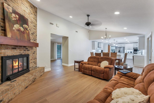 living room with a fireplace, ceiling fan with notable chandelier, light hardwood / wood-style flooring, and lofted ceiling