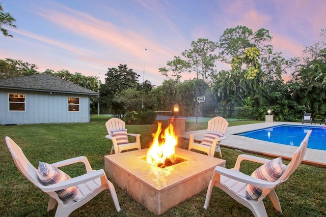 pool at dusk featuring an outdoor fire pit and a lawn