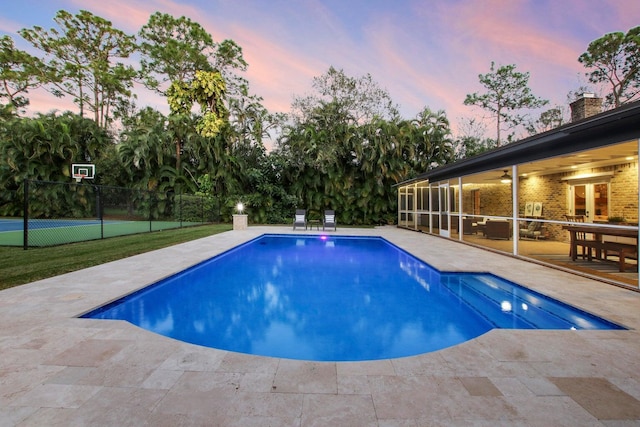 pool at dusk with ceiling fan, tennis court, and a patio