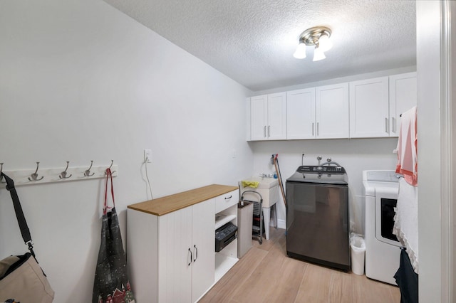 washroom with washer and dryer, a textured ceiling, light wood-type flooring, and cabinets