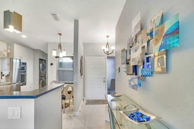 kitchen featuring a notable chandelier, hanging light fixtures, stacked washing maching and dryer, appliances with stainless steel finishes, and light tile patterned floors