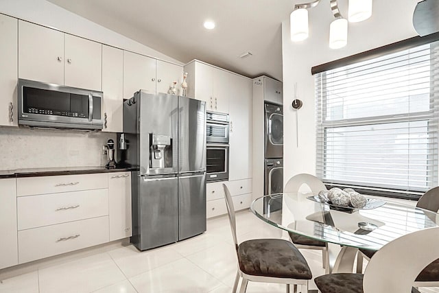 kitchen featuring stacked washer and clothes dryer, stainless steel appliances, light tile patterned flooring, hanging light fixtures, and white cabinets