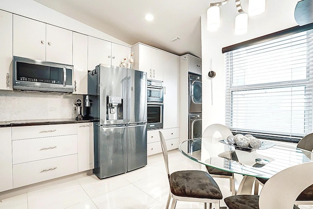6140 Kings Gate Cir, Delray Beach, FL 33484 - kitchen with appliances with stainless steel finishes, stacked washing machine and dryer, backsplash, light tile patterned flooring, and white cabinets