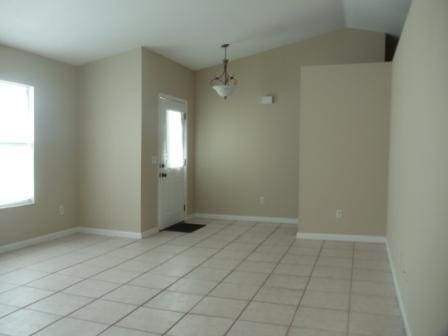 tiled spare room featuring a chandelier, vaulted ceiling, and a healthy amount of sunlight