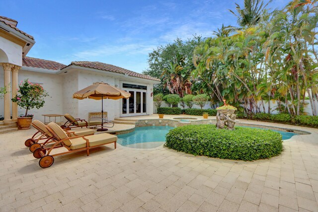outdoor pool with an in ground hot tub, french doors, and a patio area