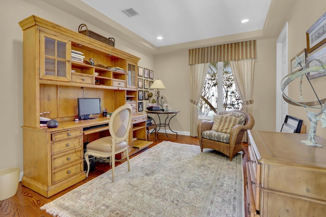 home office with visible vents, baseboards, built in study area, and wood finished floors
