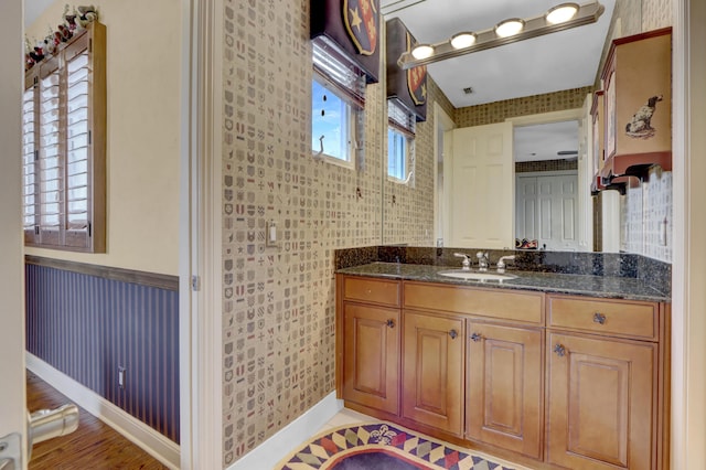 bathroom with vanity, baseboards, wallpapered walls, and visible vents