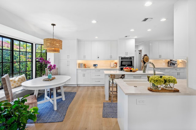 kitchen featuring light stone countertops, sink, stainless steel double oven, pendant lighting, and white cabinets