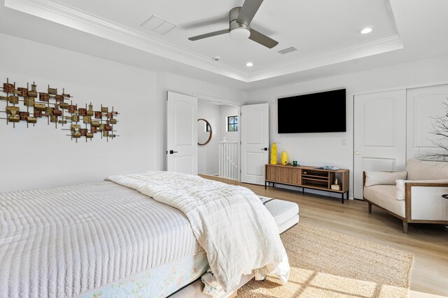 bedroom featuring light wood-type flooring, a tray ceiling, ceiling fan, and crown molding