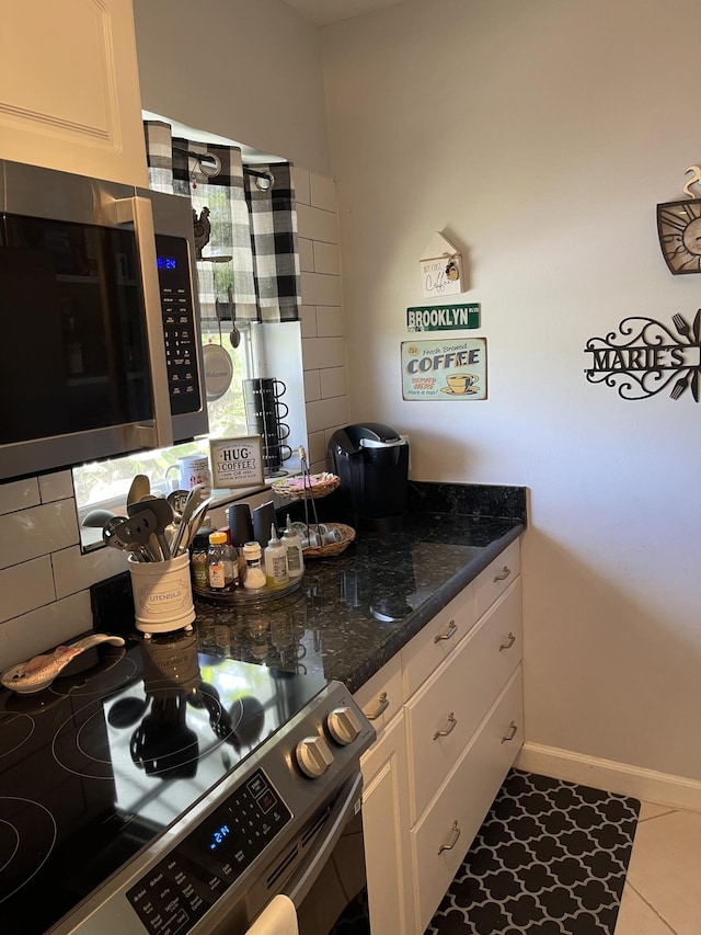 kitchen with dark stone counters, white cabinets, decorative backsplash, light tile patterned floors, and stainless steel appliances