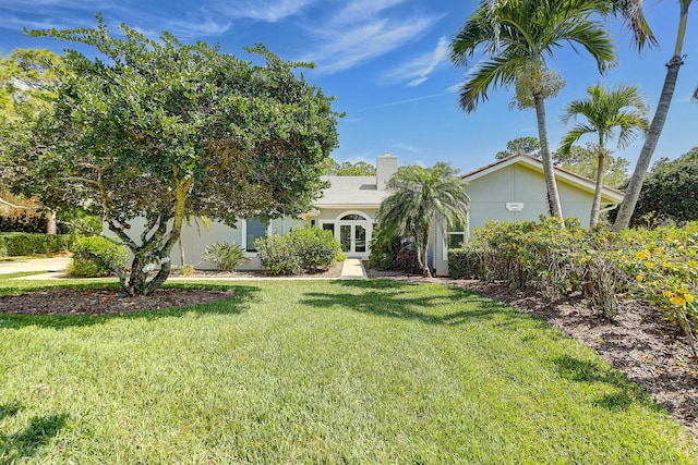 view of property hidden behind natural elements featuring french doors and a front lawn