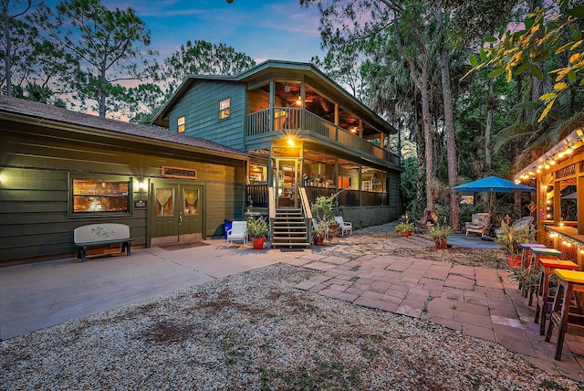 back house at dusk featuring a patio, a balcony, and an outdoor bar