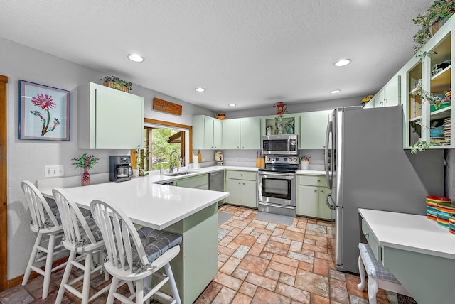 kitchen with kitchen peninsula, a textured ceiling, stainless steel appliances, sink, and a breakfast bar area