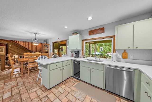 kitchen with dishwasher, sink, wooden walls, green cabinetry, and kitchen peninsula