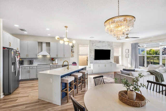 dining space with a textured ceiling, ceiling fan with notable chandelier, light wood-type flooring, and sink