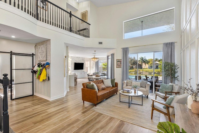 living room with a barn door, light hardwood / wood-style floors, a high ceiling, and a notable chandelier