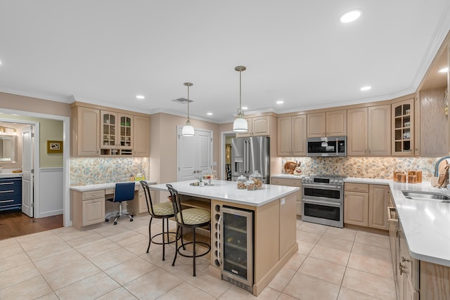 kitchen with light brown cabinetry, appliances with stainless steel finishes, sink, ornamental molding, and a center island with sink