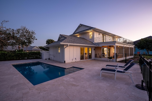 back house at dusk featuring a fenced in pool, a balcony, and a patio area