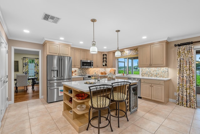 kitchen featuring appliances with stainless steel finishes, a kitchen island, light brown cabinets, ornamental molding, and light tile patterned flooring