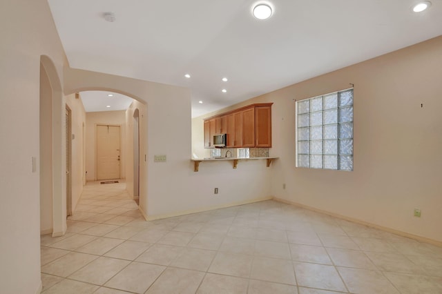 kitchen with light stone countertops, kitchen peninsula, a breakfast bar area, and light tile patterned floors