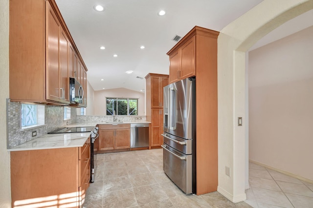 kitchen featuring backsplash, sink, vaulted ceiling, light stone countertops, and appliances with stainless steel finishes